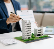 Commercial Property Insurance concept with a man with a pen pointing to model business buildings on desk.