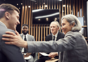 Professional Liability as a group of diverse business people sitting at a table with Asian woman congratulating a young man.