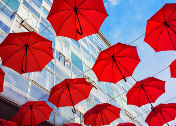 Commercial Umbrella Policy concept with red umbrellas flying up in the air in front of a business building.