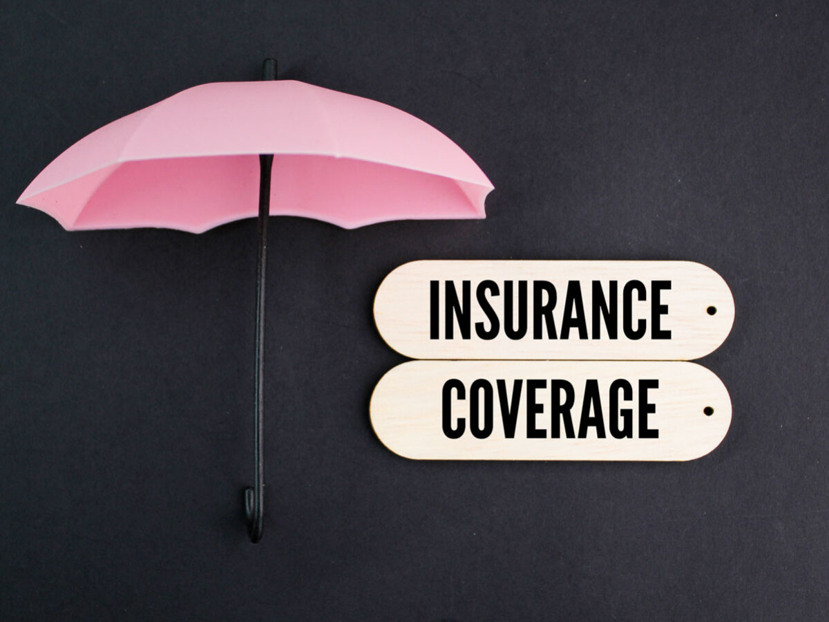 Pink umbrella with the words "insurance coverage" on white little boards.
